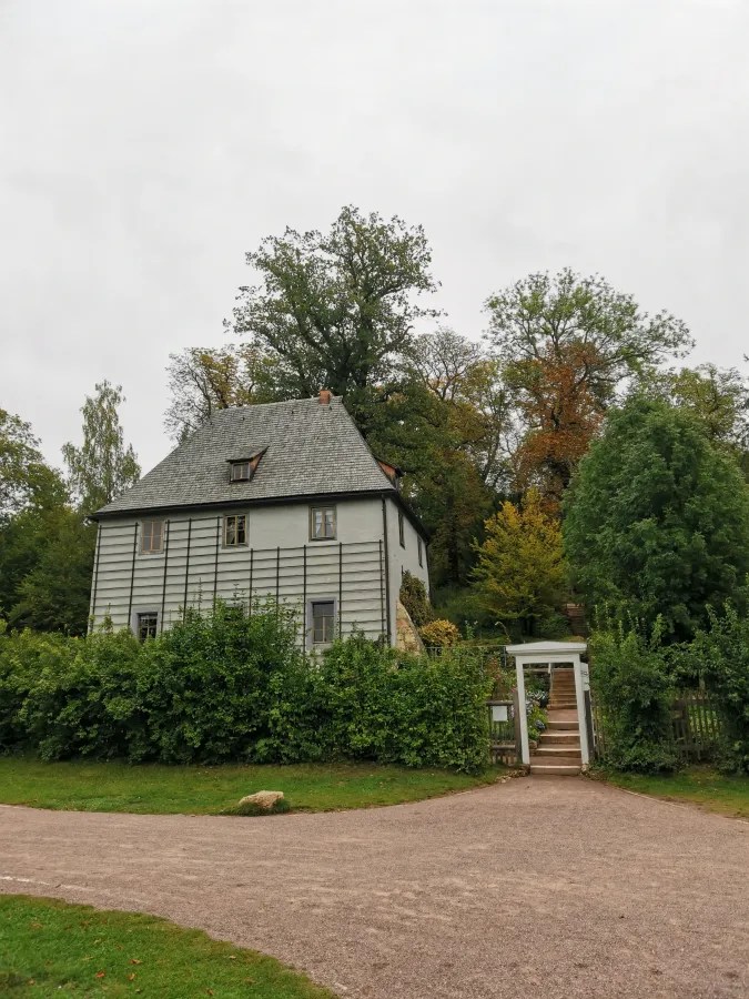 Das Gartenhaus von Johann Wolfgang Goethe in Weimar, umgeben von üppigem Grün und Bäumen, an einem bewölkten Tag.