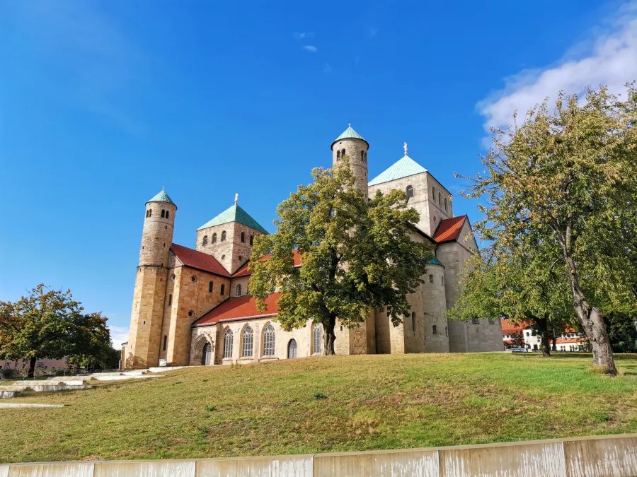 A historical church with towers and a green roof, surrounded by trees and grass under a clear blue sky.