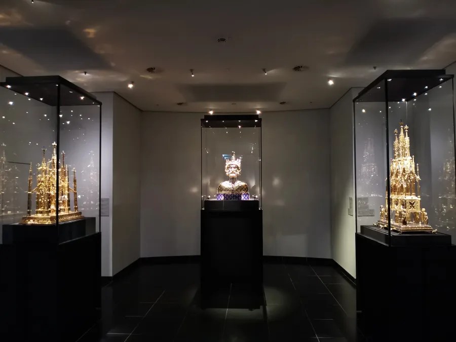 Innenansicht eines Ausstellungsraums mit mehreren Vitrinen, die goldene Kunstwerke und Reliquiare beherbergen.