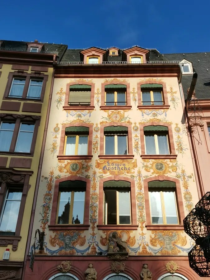 Fassade eines historisch verzierten Fachwerkhauses in Mainz mit bunten Fenstern und kunstvollen Malereien.