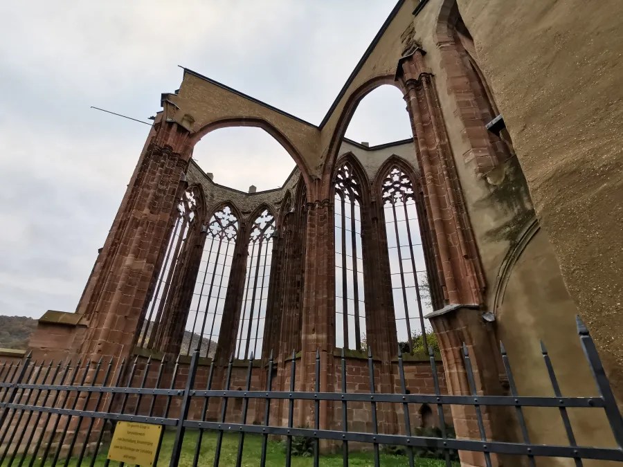 Ruine der Wernerkapelle mit steinernen Wänden und gotischen Fenstern, umgeben von einem Zaun, unter einem bewölkten Himmel.