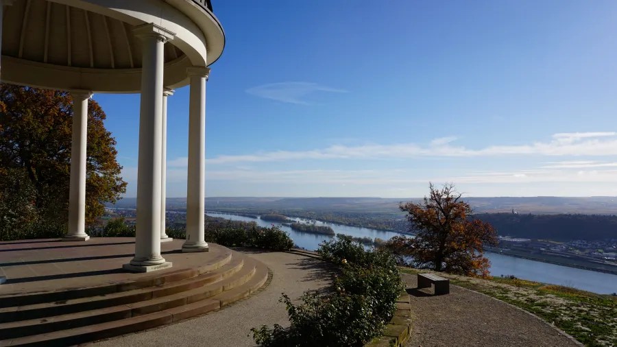 Blick auf das Rheintal von einem Anblickspunkt mit einer Säulenstruktur im Vordergrund und bunten Bäumen.