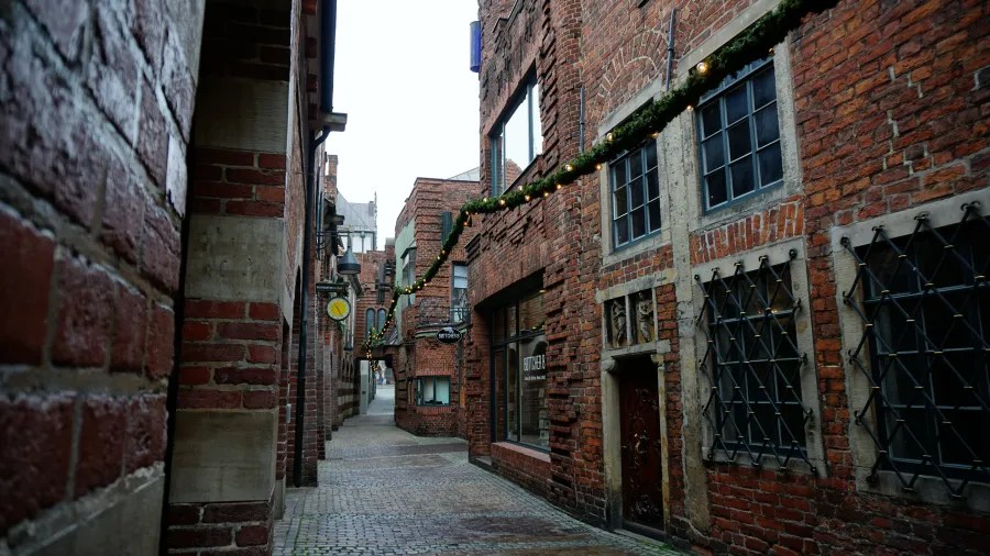 Eine enge Gasse mit roten Backsteinmauern und Fenstern, die in eine ruhige, charmante Atmosphäre eintaucht.