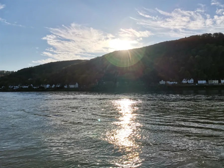Sonnenaufgang über dem Rhein mit einer ruhigen Wasseroberfläche und malerischer Hügelkulisse im Hintergrund.