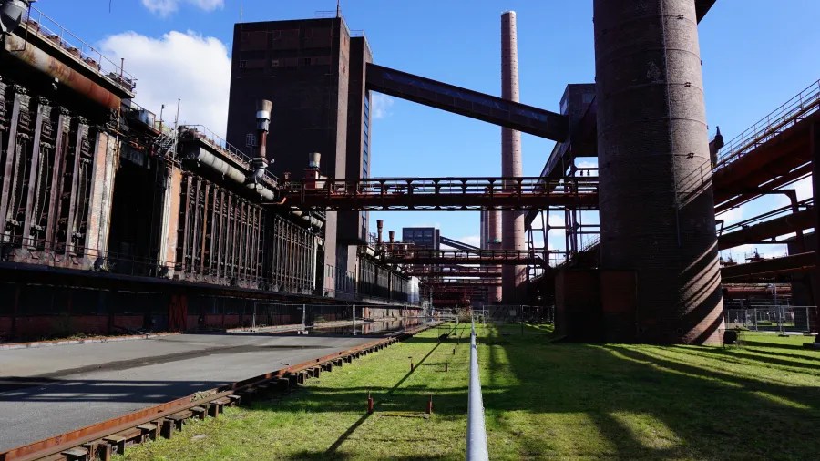 Industriekultur und Architektur der Zeche Zollverein mit großen Schornsteinen und Stahlkonstruktionen vor einem blauen Himmel.