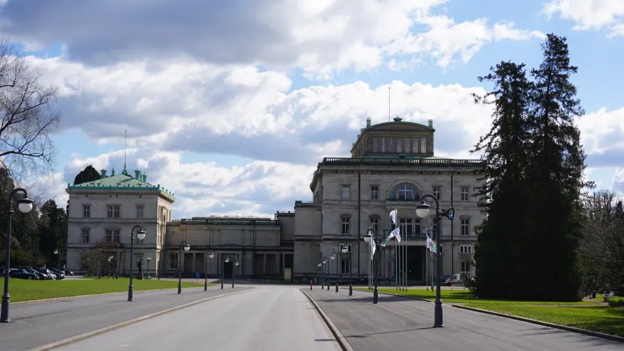 Die Villa Hügel mit ihrer imposanten Architektur und dem gepflegten Umfeld, umgeben von Bäumen und einer grünen Landschaft, unter strahlend blauem Himmel.