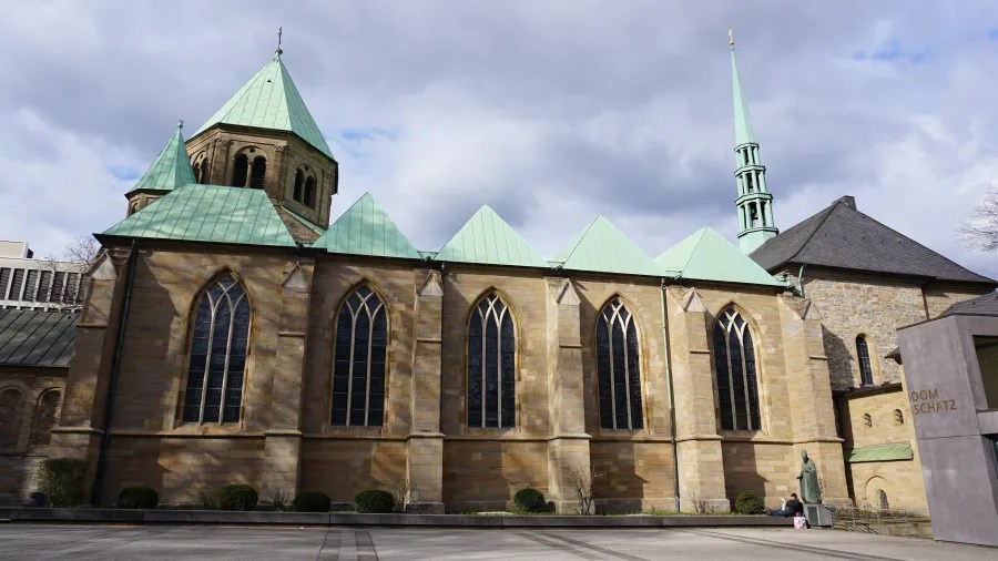 Außenansicht der Alten Synagoge in Essen mit einem großen Turm und grünen Dächern, umgeben von einer klaren, bewölkten Himmel.