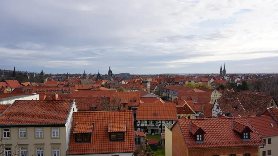 Panoramic view of a town with red-tiled roofs under a cloudy sky.