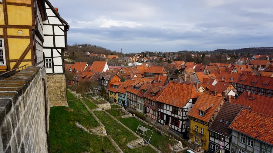 Panoramic view of a quaint village with timber-framed houses and red roofs, surrounded by greenery under a cloudy sky.