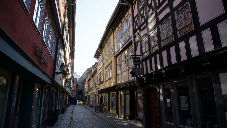 A narrow street lined with historic half-timbered buildings, featuring a mix of colors and architectural details, illuminated by natural light.