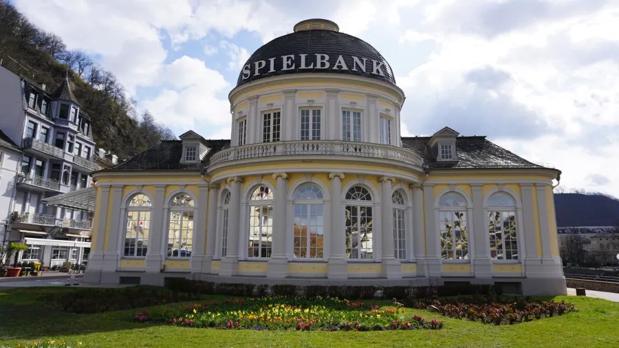 Das Gebäude der Spielbank in Bad Ems mit einem runden Dach, großen Fenstern und einem schön gestalteten Blumenbeet im Vordergrund.
