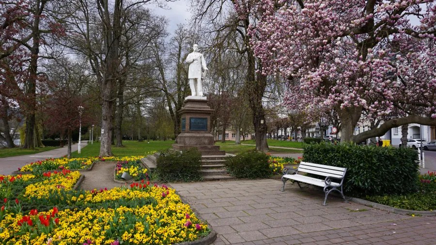 Ein Denkmal in einem Park mit bunten Blumen und blühenden Bäumen, das eine ruhige und malerische Atmosphäre vermittelt.