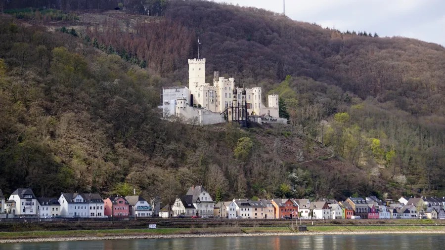 Blick auf die Marksburg, eine majestätische Burg auf einem Hügel, mit historischen Häusern am Flussufer darunter.