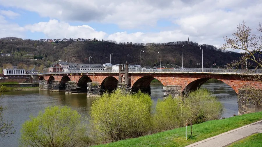 Die Römerbrücke in Trier, eine der ältesten Brücken Deutschlands, mit historischem Mauerwerk und üppigem Grün im Vordergrund.