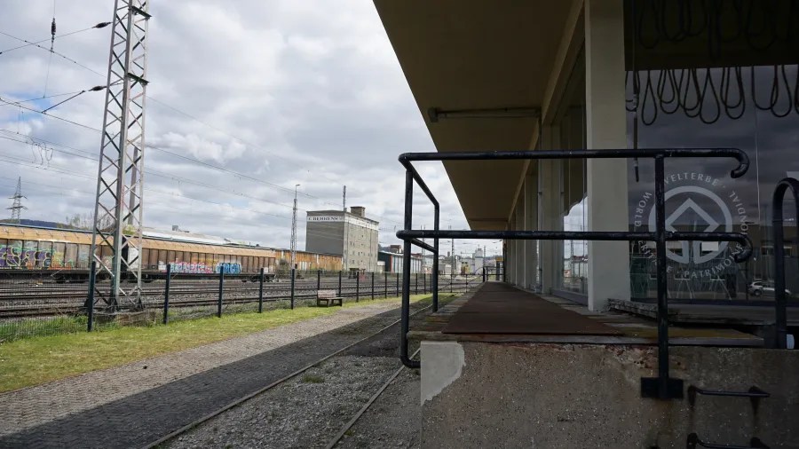 Ansicht des alten Werksbahnhofs mit Gleisen und einer graffitibedeckten Lagerhalle im Hintergrund.