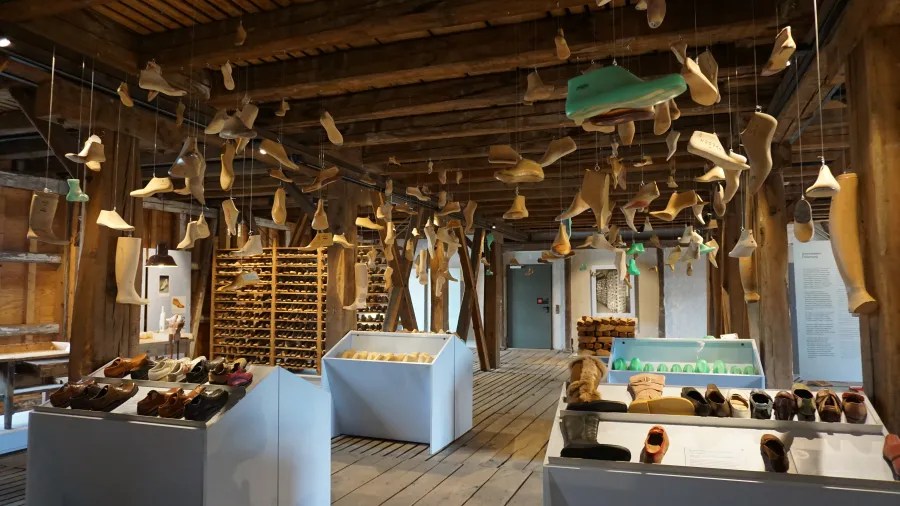 Innenansicht des Museums im Fagus-Werk mit zahlreichen Schuhleisten aus Holz, die von der Decke hängen und auf Tischen präsentiert werden, umgeben von einer rustikalen Holzarchitektur.