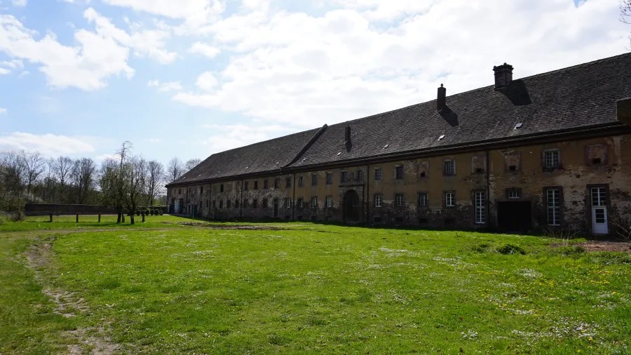 A large, old building with a sloped roof, situated on a grassy field under a partly cloudy sky.
