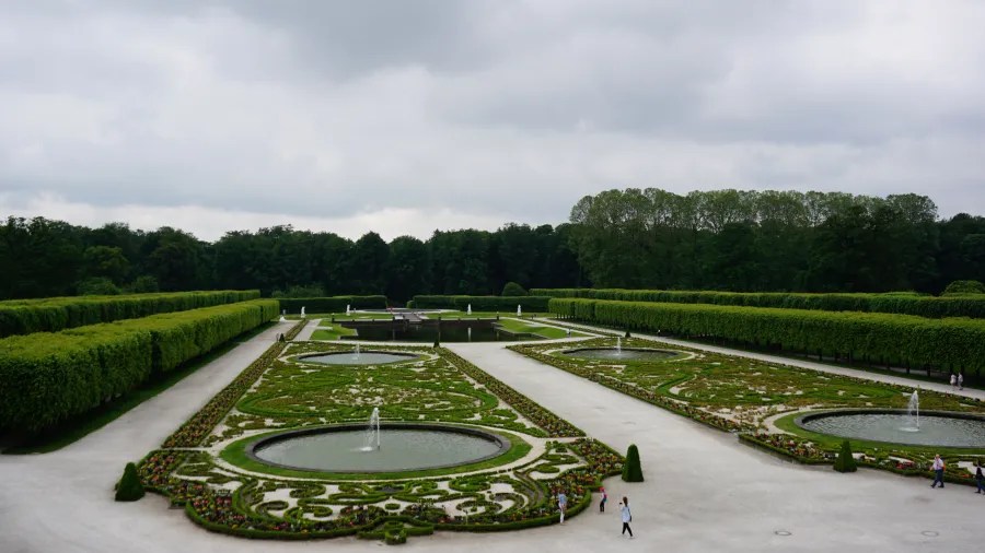 Blick auf den barocken Garten des Schlosses Augustusburg in Brühl mit geometrischen Hecken und dekorativen Wasserfontänen.