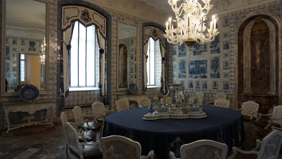 Elegantem Innenraum eines Schlosses mit einem runden Tisch und Stühlen, geschmückt mit blauen Fliesen, Spiegeln und einem Kristalllüster.