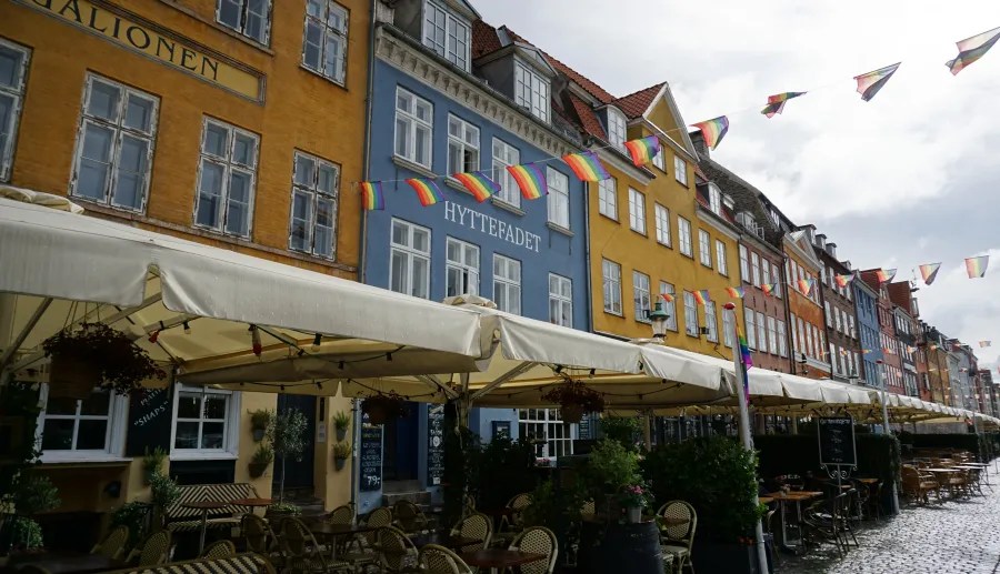 Bunte Häuserfassaden mit Regenbogenflaggen in Kopenhagen, die ein lebendiges Straßenbild und eine einladende Atmosphäre schaffen.
