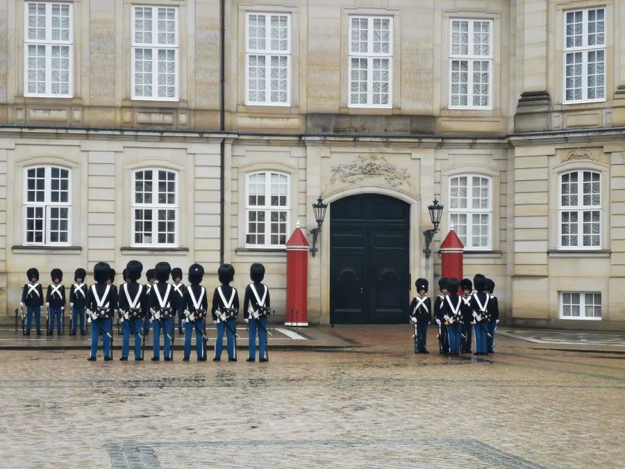 Eine Gruppe von Wachen in traditionellen Uniformen steht vor einem historischen Gebäude mit auffälligen Fenstern und einer großen, dunklen Tür.