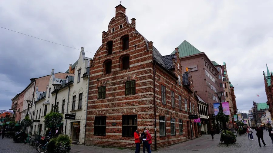Historisches Gebäude in Kopenhagen mit rot-weißen Ziegeln, umgeben von modernen und alten Gebäuden, unter einem bewölkten Himmel.