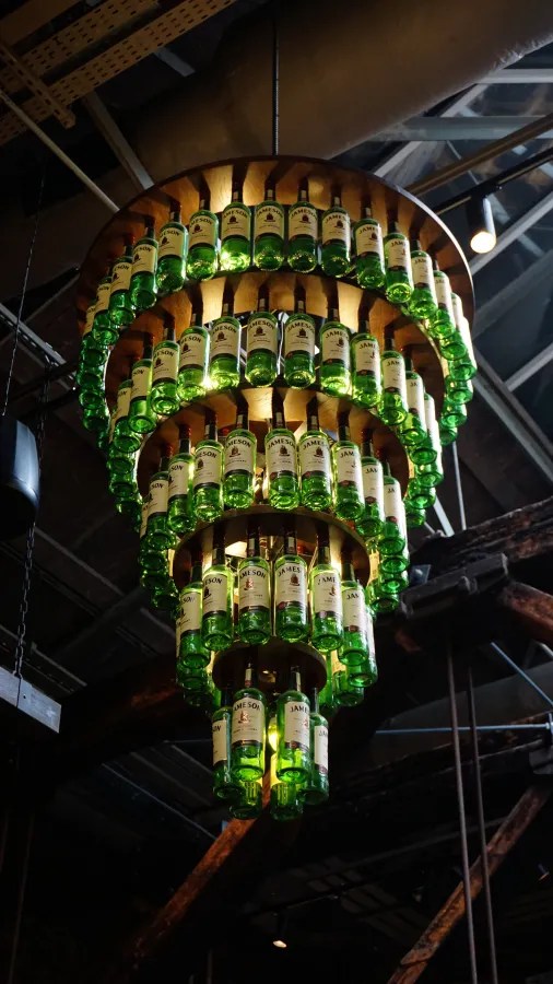 Ein beleuchteter Kronleuchter aus grünen Jameson Whiskey-Flaschen in einem stilvollen Innenraum.