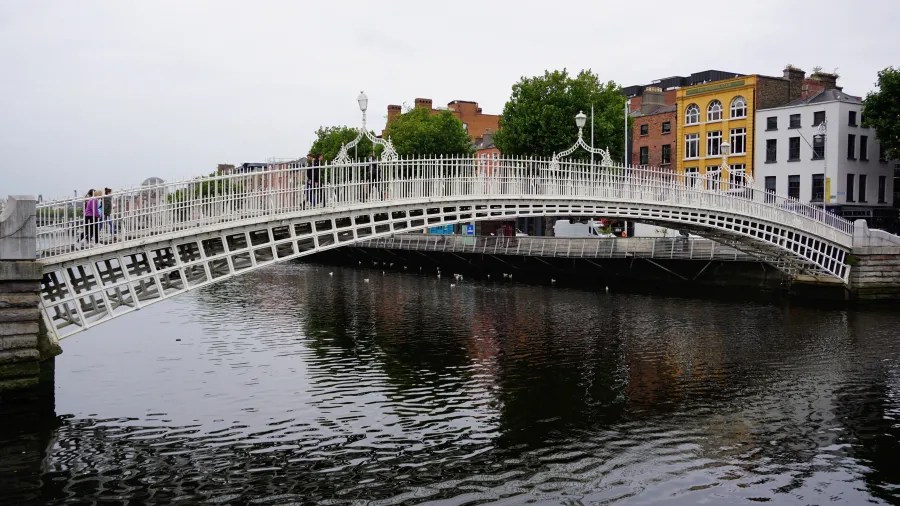 Die Ha'Penny Bridge in Dublin, eine symbolträchtige weiße Fußgängerbrücke, die über den River Liffey führt, umgeben von typischen irischen Gebäuden.