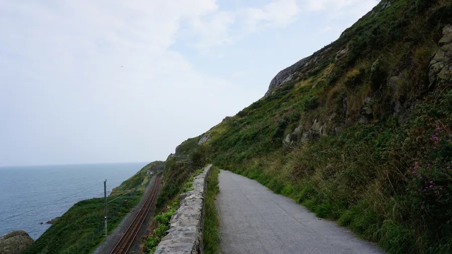 Ein malerischer Küstenweg entlang der Klippen mit Blick auf den Atlantik, bewachsen mit grünem Gras und umgeben von steilen Hängen.