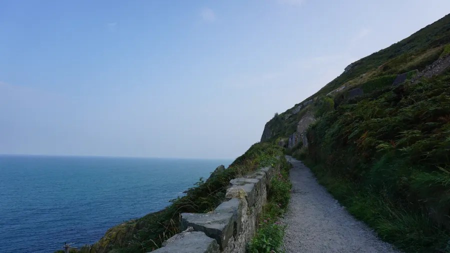Ein schmaler Weg führt entlang der Klippen, mit Blick auf den ruhigen Atlantischen Ozean und den klaren Himmel.