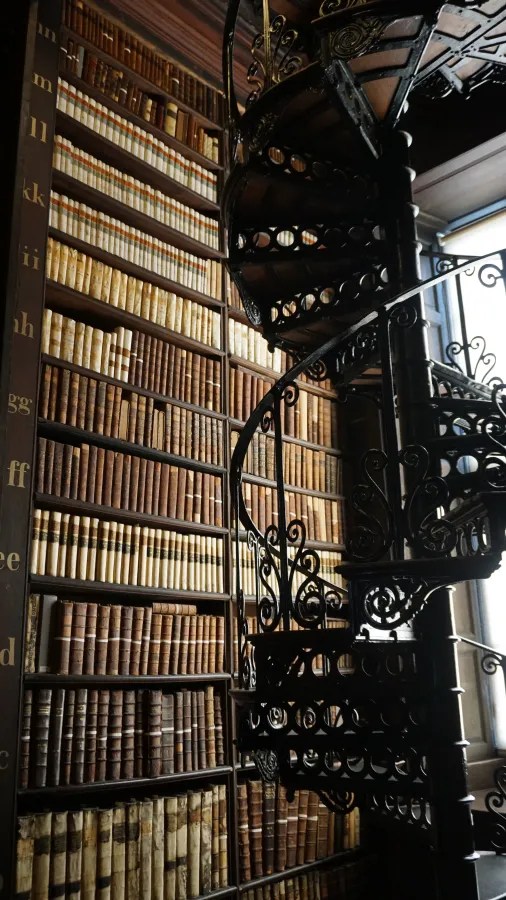 Eine spiralförmige Treppe in einer alten Bibliothek, umgeben von Regalen voller antiker Bücher.