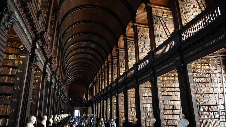 Der Long Room im Trinity College, Dublin, zeigt hohe Regale voller Bücher und elegant gestaltete Details mit Statuen an den Seiten.