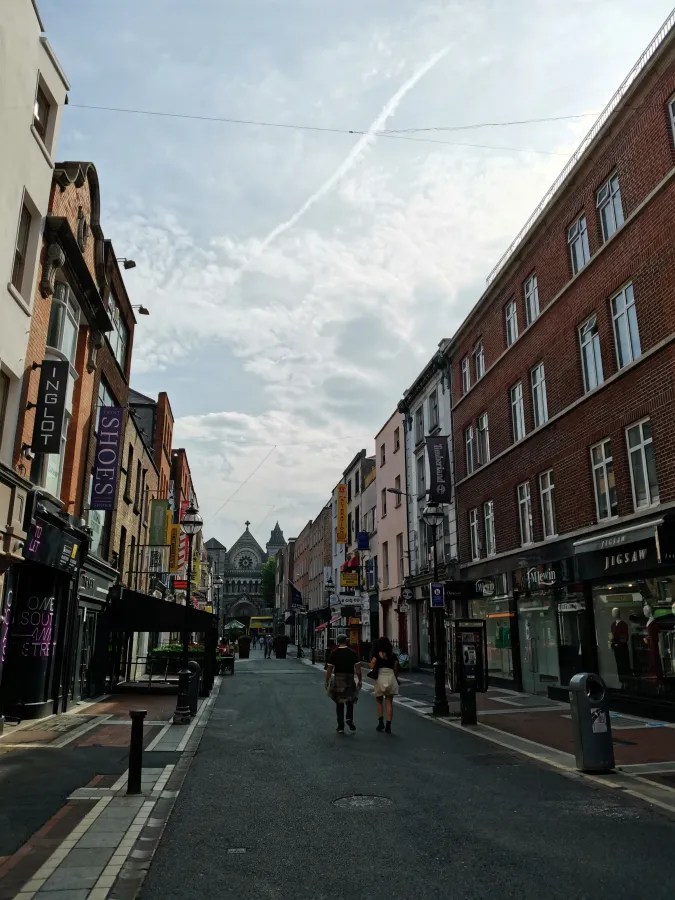 Blick auf eine belebte Straße in Dublin mit verschiedenen Geschäften und einem klaren Himmel.