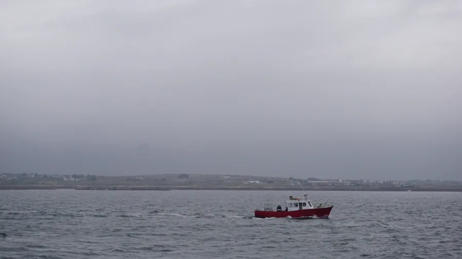Ein rotes Boot fährt über das ruhige Wasser der Irischen See, mit einer bewölkten Himmel im Hintergrund.