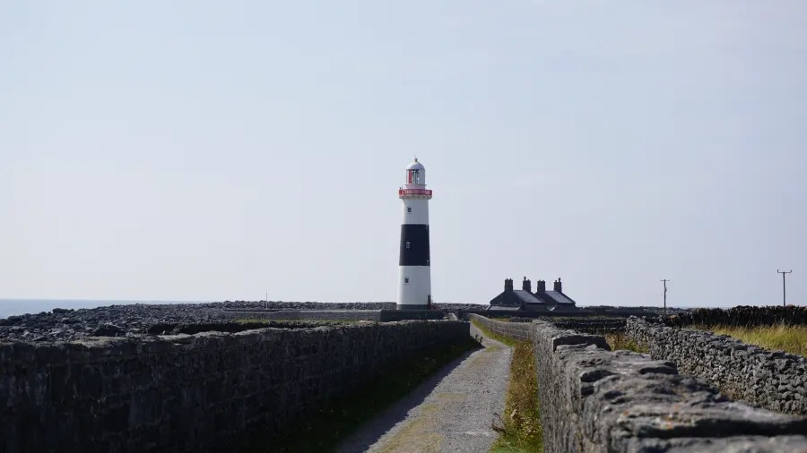 Ein Leuchtturm auf der irischen Insel Inis Oírr, umgeben von Steinmauern und einem klaren Himmel.