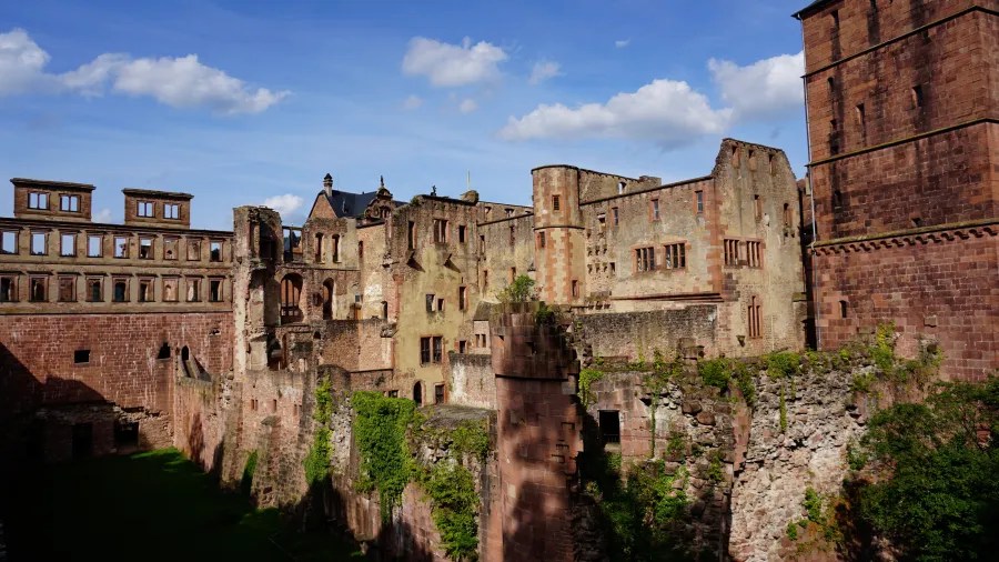 Ruinenansicht des Heidelberger Schlosses mit beeindruckender Architektur und grüner Vegetation vor einem blauen Himmel.