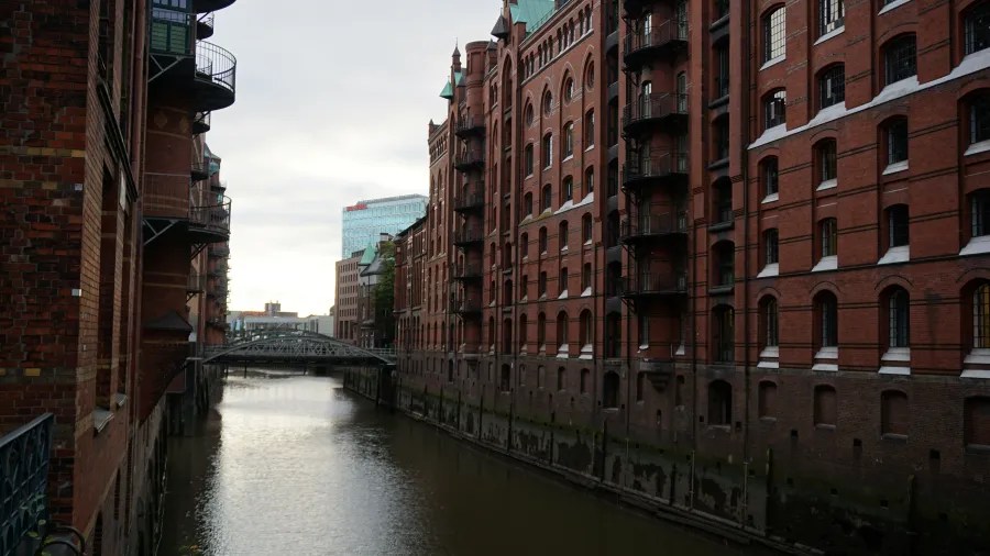 Ansicht von roten Backsteingebäuden entlang eines Kanals in Hamburg, Deutschland, mit Brücke im Hintergrund.