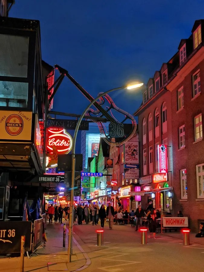 Beleuchtete Straße in Hamburgs Reeperbahn mit bunten Neonlichtern und Menschen, die gesellig unterwegs sind.
