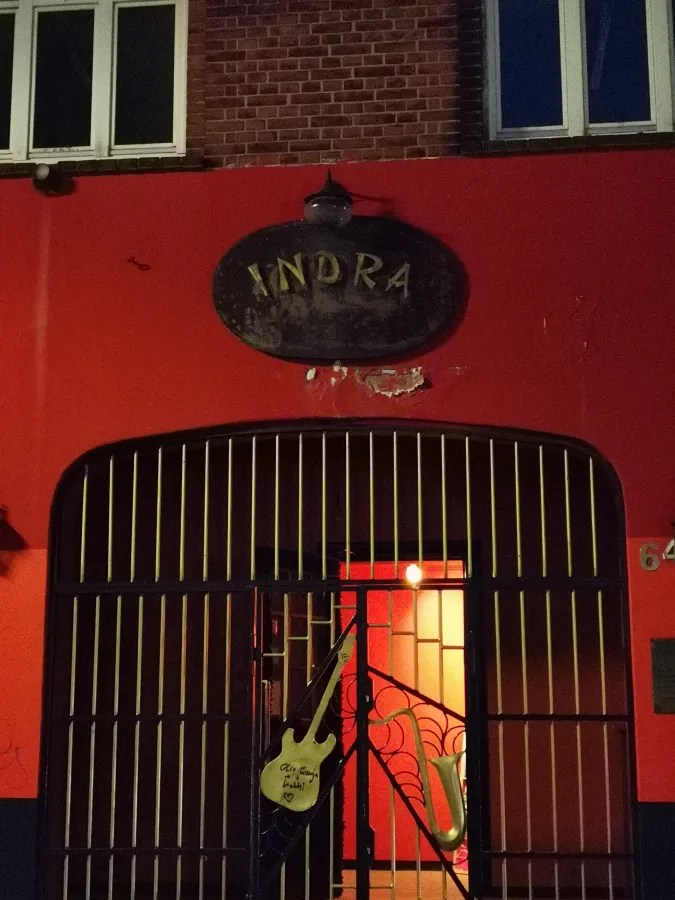 Eingang des Indra, einem berühmten Musikclub in Hamburg, mit roter Wand und einem Gitarrensymbol am Tor.
