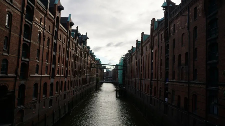 Blick auf die Speicherstadt in Hamburg mit alten Backsteingebäuden, die entlang eines Kanals angeordnet sind, unter einem bewölkten Himmel.