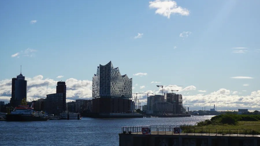 Blick auf die Elbphilharmonie in Hamburg, umgeben von moderner Architektur und dem Wasser der Elbe, bei klarem blauen Himmel.