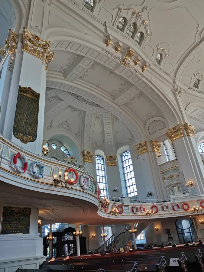 Blick auf die Innenarchitektur der Hauptkirche St. Michaelis in Hamburg mit goldenen Verzierungen, hohen Fenstern und einer Galerie mit Rettungsringen.