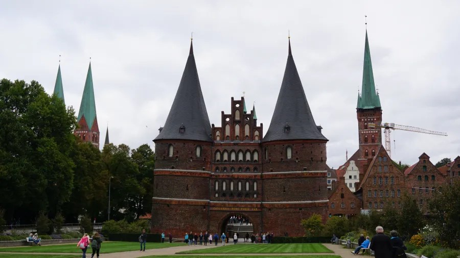 Die historische Lübecker Holstentor mit seinen markanten Türmen und Backsteinarchitektur, umgeben von Besuchern und Grünflächen.