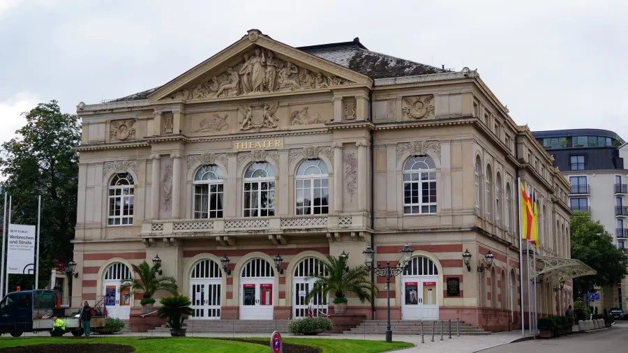 Fassade des Theaters in Baden-Baden mit kunstvollen Verzierungen und Säulen, umgeben von Bäumen und einer gepflegten Umgebung.