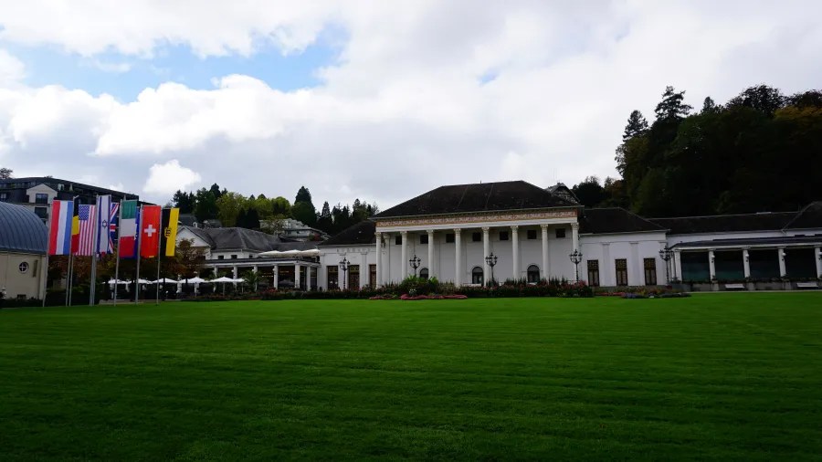 Blick auf das elegante Kurhaus von Baden-Baden, umgeben von einer großzügigen Rasenfläche und geflaggt mit internationalen Flaggen unter einem bewölkten Himmel.