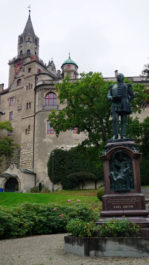 Statue of Karl Anton in front of a historic castle with a tower and surrounding greenery.