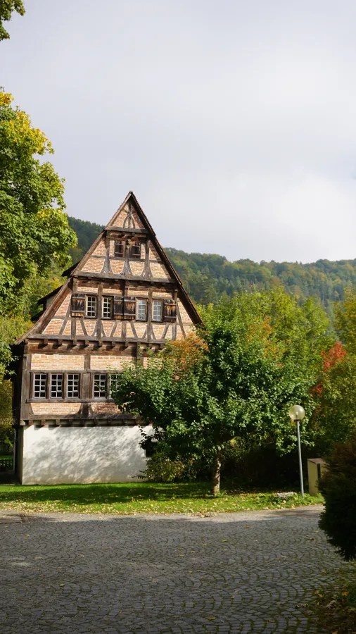 Historisches Fachwerkhaus umgeben von Bäumen und einer ruhigen Gartenlandschaft in Blaubeuren, Deutschland.