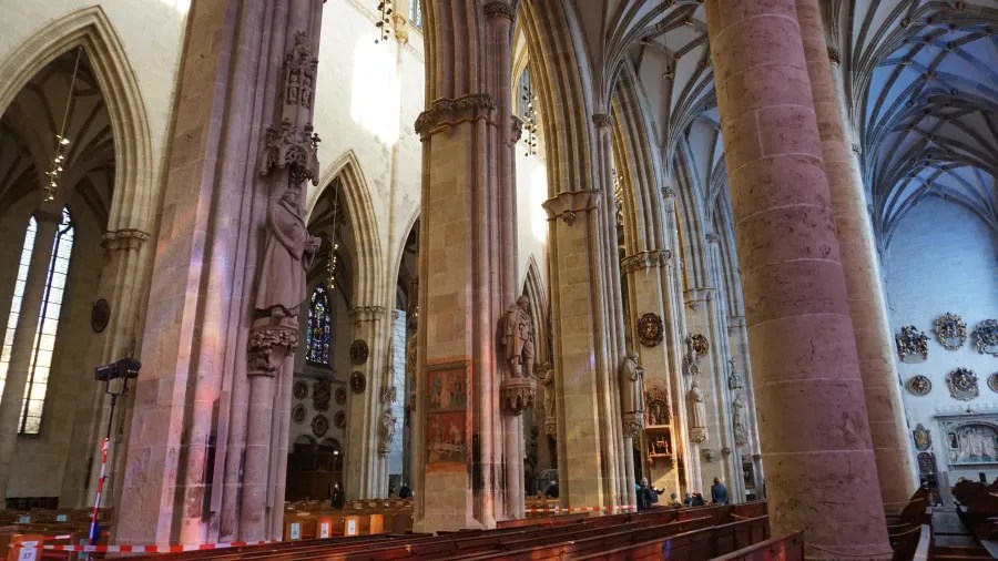 Inner view of a Gothic church in Ulm, featuring tall columns, stained glass windows, and wooden pews.