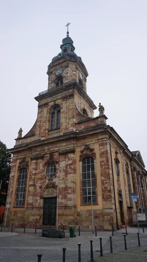 Die Ansicht einer alten Kirche in Saarbrücken mit einem markanten Turm und einem detailreichen Fassadendesign.