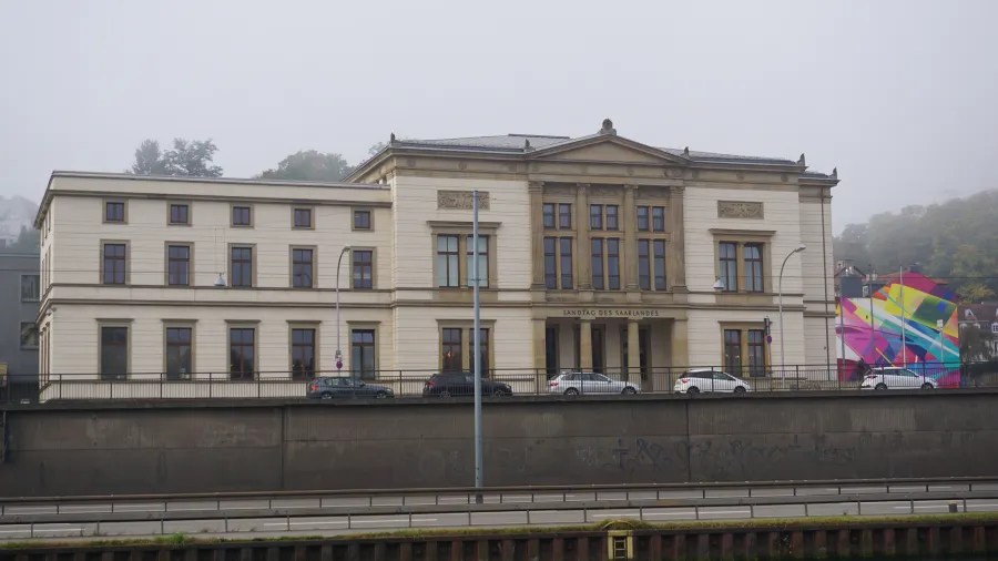Historisches Gebäude des Landtags des Saarlandes in Saarbrücken, umgeben von Nebel und modernen Kunstwerken.